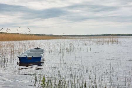 Small fishing boat anchored in a forest lake. Reflections on water. Transportation, traditional craft, recreation, leisure activity, healthy lifestyle, local tourism concepts. Spring landscapeの写真素材