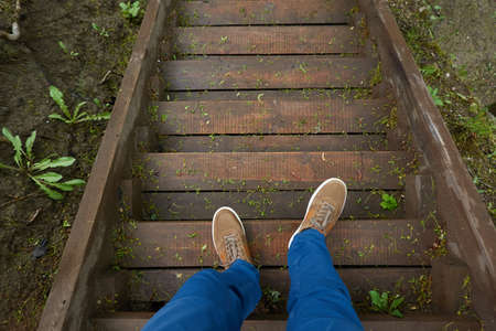 Man standing on a modern wooden stairway (boardwalk). Blue jeans, brown boots. Forest park. Spring, early summer. Nature, tourism, hiking, nordic walking, recreation, healthy lifestyleの写真素材