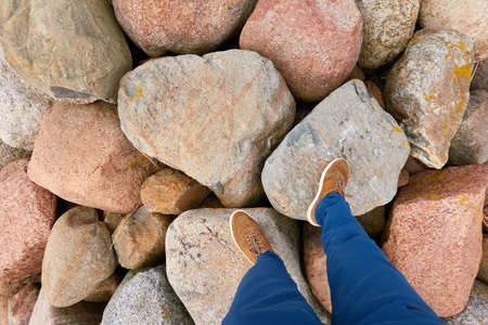 A man in blue jeans and brown boots standing on large stones (breakwaters). Baltic sea shore....