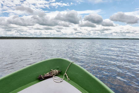 Rowing a small green boat on the forest lake. Dramatic sky. Reflections on water. Transportation, traditional craft, recreation, leisure activity, healthy lifestyle, local tourism conceptsの写真素材