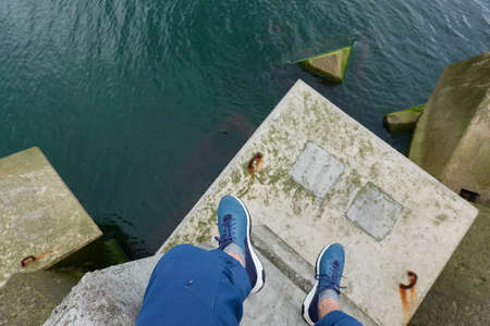 Man sitting on breakwaters. Blue jeans, trekking boots. Sea water surface texture. Turquoise tones....