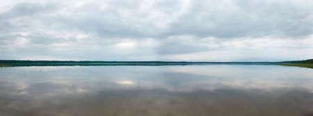 Panoramic view from the shore of a crystal clear forest lake (river). Dramatic sky, glowing storm...