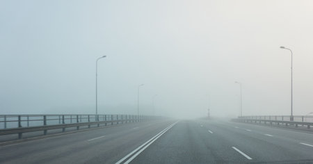 An empty asphalt road bridge (highway) in a thick fog. Pedestrian walkway, crossing, street lights. Dangerous driving, walking, cycling, traffic laws conceptsの写真素材