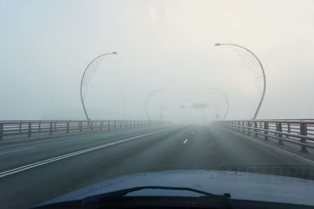 An empty asphalt road bridge (highway) in a thick fog. Pedestrian walkway, crossing, street lights. Dangerous driving, walking, cycling, traffic laws conceptsの写真素材