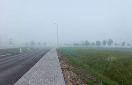 An empty new asphalt road (hghway) in a thick fog. Red and white roadblocks. Concept landscape. Transportation, dangerous driving, safety, traffic laws, remote places conceptsの写真素材