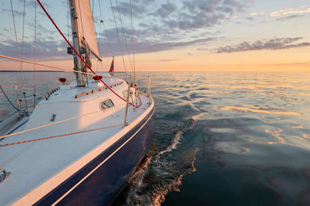 Yacht sailing in an open Baltic sea at sunset. Top down view of the deck and mast. Clear sky, golden sunlight. Waves, water splashes. Travel, cruise, sport, recreation, vacationsの写真素材