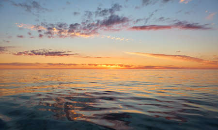 Panoramic view from the Baltic sea shore at sunset. Clear sky, glowing clouds, golden sunlight, water surface texture. Nature, environment. Idyllic dreamlike seascapeの写真素材