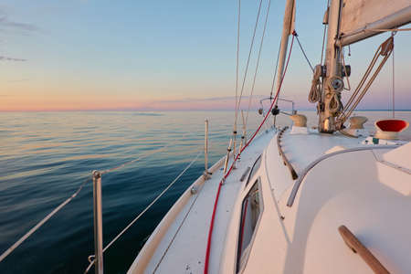 White yacht sailing on a sunny summer day. View of the deck, mast, sails. Waves and water splashes. Clear sunset sky. Baltic sea. Transportation, cruise, sport, recreation, wanderlust conceptsの写真素材