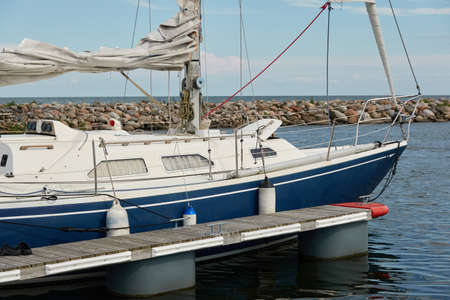 Sloop rigged sailboat (for rent and sale) moored to a pier in a yacht marina. Baltic sea. Nautical vessel, transportation, amateur sailing, summer vacations, cruising, recreation conceptsの写真素材