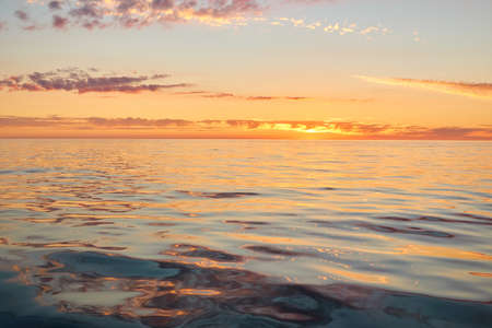 Panoramic view from the Baltic sea shore at sunset. Clear sky, glowing clouds, golden sunlight, water surface texture. Nature, environment. Idyllic dreamlike seascapeの写真素材