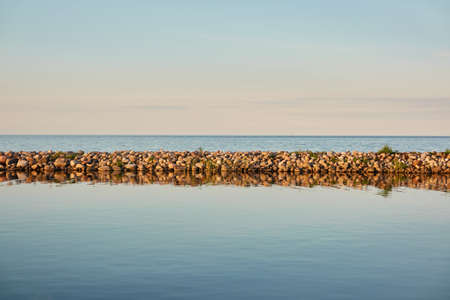 Baltic sea on a clear summer day, panoramic view. Clear sunset sky, reflections on water. Stones, breakwaters. Ruhnu island, Estonia. Nature, eco tourism, travel destinations, recreation themesの写真素材