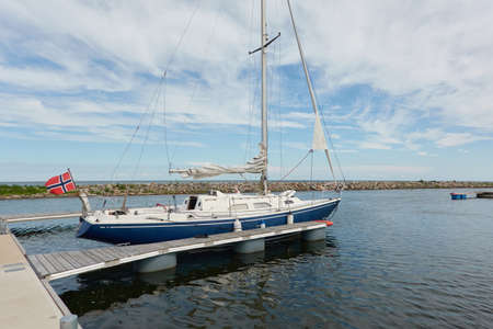 Sloop rigged sailboat (for rent and sale) moored to a pier in a yacht marina. Baltic sea. Nautical vessel, transportation, amateur sailing, summer vacations, cruising, recreation conceptsの写真素材
