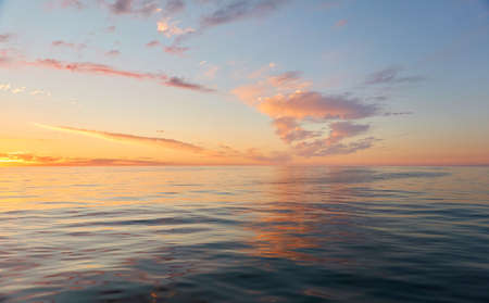 Panoramic view from the Baltic sea shore at sunset. Clear sky, glowing clouds, golden sunlight, water surface texture. Nature, environment. Idyllic dreamlike seascapeの写真素材