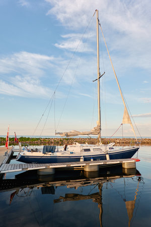 Sloop rigged sailboat (for rent and sale) moored to a pier in a yacht marina. Baltic sea. Nautical vessel, transportation, amateur sailing, summer vacations, cruising, recreation conceptsの写真素材