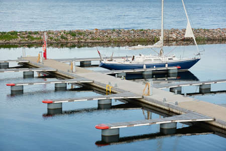 Sloop rigged sailboat (for rent and sale) moored to a pier in a yacht marina. Baltic sea. Nautical vessel, transportation, amateur sailing, summer vacations, cruising, recreation conceptsの写真素材