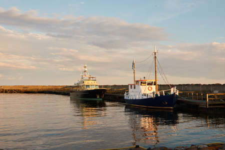 Small ships (fishing boats) moored to a pier in yacht marina at sunset. Ruhnu island, Estonia, Baltic sea. Nautical vessel, transportation, traditional craft themesの写真素材
