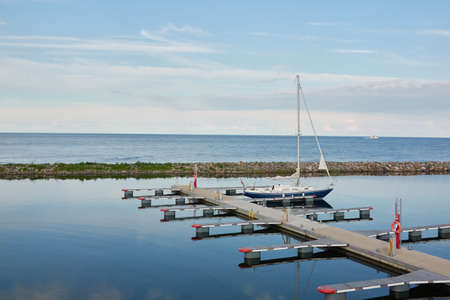 Sloop rigged sailboat (for rent and sale) moored to a pier in a yacht marina. Baltic sea. Nautical vessel, transportation, amateur sailing, summer vacations, cruising, recreation conceptsの写真素材