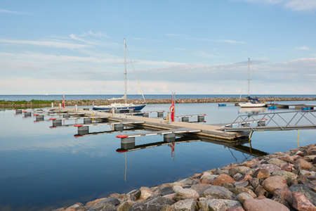 Sloop rigged sailboat (for rent and sale) moored to a pier in a yacht marina. Baltic sea. Nautical vessel, transportation, amateur sailing, summer vacations, cruising, recreation conceptsの写真素材