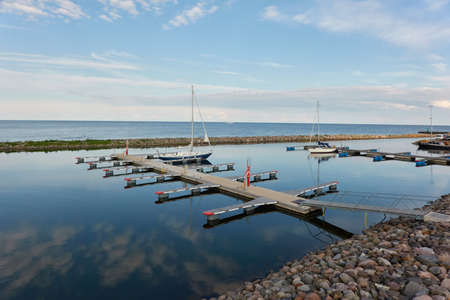 Sloop rigged sailboat (for rent and sale) moored to a pier in a yacht marina. Baltic sea. Nautical vessel, transportation, amateur sailing, summer vacations, cruising, recreation conceptsの写真素材