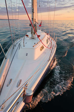 Yacht sailing in an open Baltic sea at sunset. Top down view of the deck and mast. Clear sky, golden sunlight. Waves, water splashes. Travel, cruise, sport, recreation, vacationsの写真素材