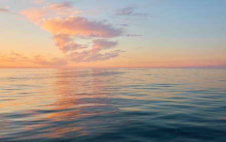 Panoramic view from the Baltic sea shore at sunset. Clear sky, glowing clouds, golden sunlight, water surface texture. Nature, environment. Idyllic dreamlike seascapeの写真素材