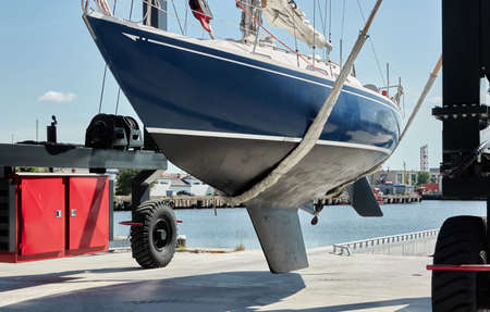 Blue sloop rigged sailboat lifted by a crane being placed back in the water after winterization....
