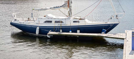 Blue sloop rigged sailboat (for rent and sale) moored to a pier in a yacht marina. Nautical vessel, transportation, amateur sailing, vacations, cruising, recreation conceptsの写真素材