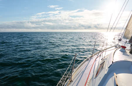 White yacht sailing on a sunny summer day. Top down (high angle) view of the deck, mast, sails. Waves and water splashes. Clear blue sky. Baltic sea. Transportation, cruise, sport, recreationの写真素材