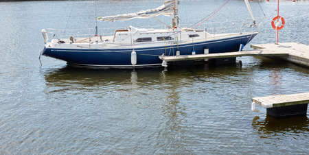 Blue sloop rigged sailboat (for rent and sale) moored to a pier in a yacht marina. Nautical vessel,...