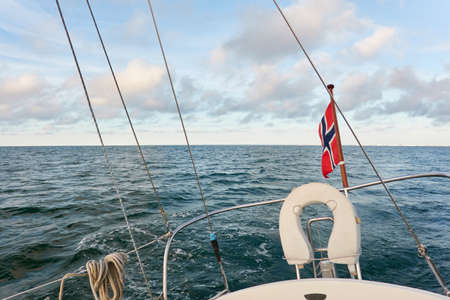 White yacht sailing at sunset. Boat side railing, winch, rigging equipment. View from the cockpit. Baltic sea. Norway flag. Transportation, leisure activity, cruise, yachting, summer vacationsの写真素材