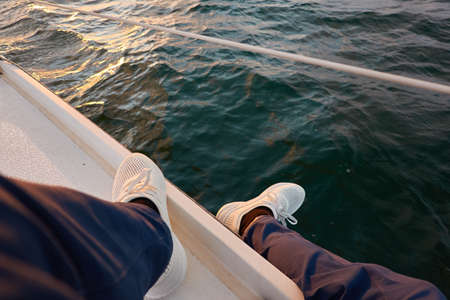 Man in a blue jeans and white boots sitting on deck of a sloop rigged yacht. Baltic sea. Healthy lifestyle, sport, recreation, cruise, vacation, regatta, sailing lessons, leisure activity, wanderlustの写真素材