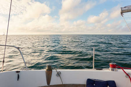White yacht sailing at sunset. Boat side railing, winch, rigging equipment. View from the cockpit. Baltic sea. Transportation, leisure activity, cruise, sport, racing, yachting, summer vacationsの写真素材