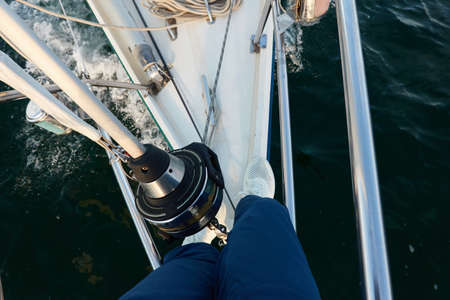 Man in a blue jeans and white boots standing on deck of a sloop rigged yacht. Baltic sea. Healthy...