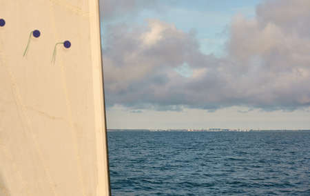 White sloop rigged yacht sailing in an open sea on a clear day. White sails against blue sky with glowing sunset clouds after the rain. Transportation, travel, cruise, sport, recreation, racingの写真素材