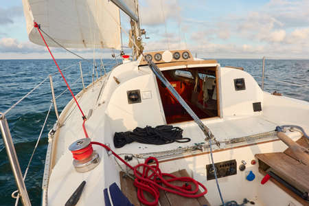 White yacht sailing at sunset. Boat side railing, winch, rigging equipment. View from the cockpit. Baltic sea. Transportation, leisure activity, cruise, sport, racing, yachting, summer vacationsの写真素材