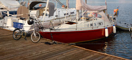 Sailboats (for rent and sale) moored to a pier in a yacht marina. Bicycle close-up. Nautical vessel, transportation, amateur sailing, summer vacations, sport, cruising, recreation conceptsの写真素材