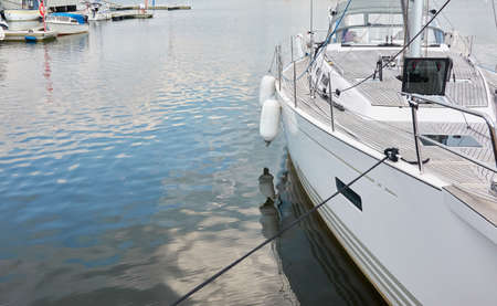 White modern sailboat (for rent and sale) moored to a pier in a yacht marina. Wooden teak deck....