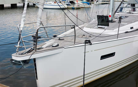White modern sailboat (for rent and sale) moored to a pier in a yacht marina. Wooden teak deck. Nautical vessel, transportation, amateur sailing, vacations, cruising, recreation conceptsの写真素材