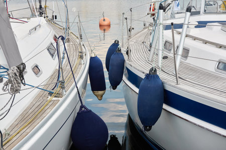 White modern sailboat (for rent and sale) moored to a pier in a yacht marina. Wooden teak deck. Nautical vessel, transportation, amateur sailing, vacations, cruising, recreation conceptsの写真素材