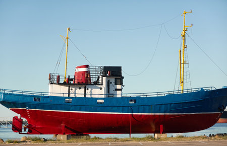 Old red blue museum fishing boat standing on land. Ventspils cargo port terminal, Latvia, Baltic sea. Past, history, industry, traditional craft, travel destinations, sightseeing themesのeditorial素材