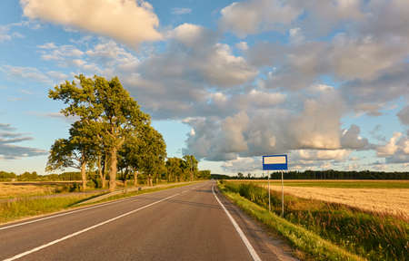 Highway (new asphalt road) through the agricultural field and forest at sunset. Dramatic sky after the thunderstorm. Summer, early autumn. Vacations, adventure, road trip, remote places. View from carの写真素材