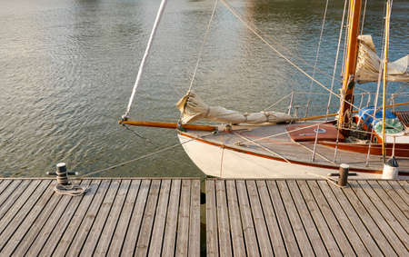Vintage wooden sailboat moored to a pier in a yacht marina. Classic retro styled sailing boat. Transportation, summer vacations, recreation, traditional craft, fishing and cruisingの写真素材