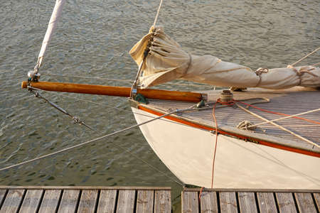 Vintage wooden sailboat moored to a pier in a yacht marina. Classic retro styled sailing boat. Transportation, summer vacations, recreation, traditional craft, fishing and cruisingの写真素材