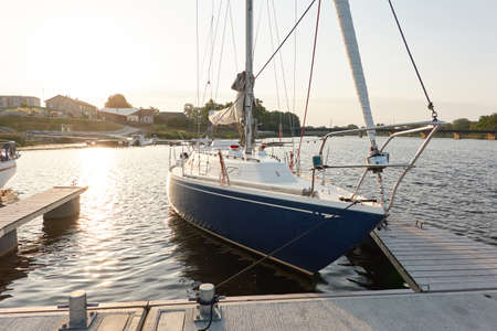 Sloop rigged sailboat (for rent and sale) moored to a pier in a yacht marina. Nautical vessel, transportation, amateur sailing, vacations, cruising, recreation conceptsの写真素材