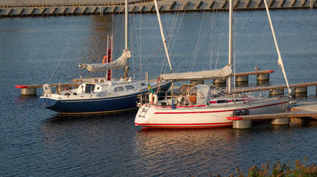 Sloop rigged sailboat (for rent and sale) moored to a pier in a yacht marina. Nautical vessel, transportation, amateur sailing, vacations, cruising, recreation conceptsの写真素材