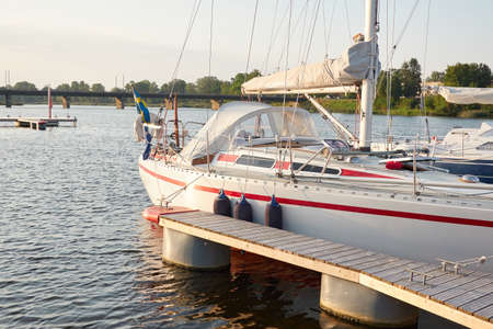 Sloop rigged sailboat (for rent and sale) moored to a pier in a yacht marina. Nautical vessel, transportation, amateur sailing, vacations, cruising, recreation conceptsの写真素材
