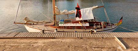 Vintage wooden sailboat moored to a pier in a yacht marina. Classic retro styled sailing boat....