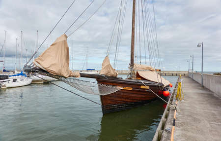 Vintage wooden sailboat moored to a pier in a yacht marina. Kuivastu harbour, Estonia. Transportation, summer vacations, recreation, amateur sailing and cruising, traditional craftの写真素材