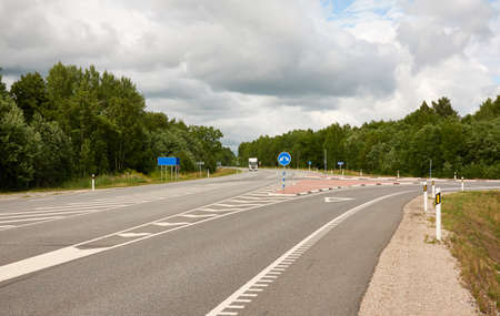 Empty highway through the forest on a sunny day. Asphalt road surface marking. Estonia, Europe. Transportation, traffic law, wanderlust, remote places, summer vacations conceptsの写真素材