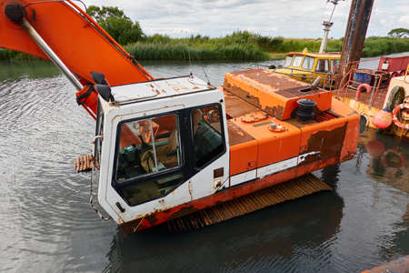 Submerged dredging excavator crane and boat in a river. Industry, special equipment, infrastructure, ecology, environmental issues, pollution conceptsの写真素材